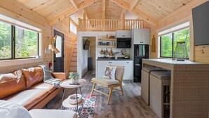 Un intérieur de chalet chaleureux avec un plafond en bois, un coin cuisine, un canapé, une table à manger et une chaise.