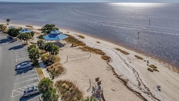 Luchtbeeld van een strand met een parkeerplaats, strandparasols en een helder uitzicht op de oceaan.