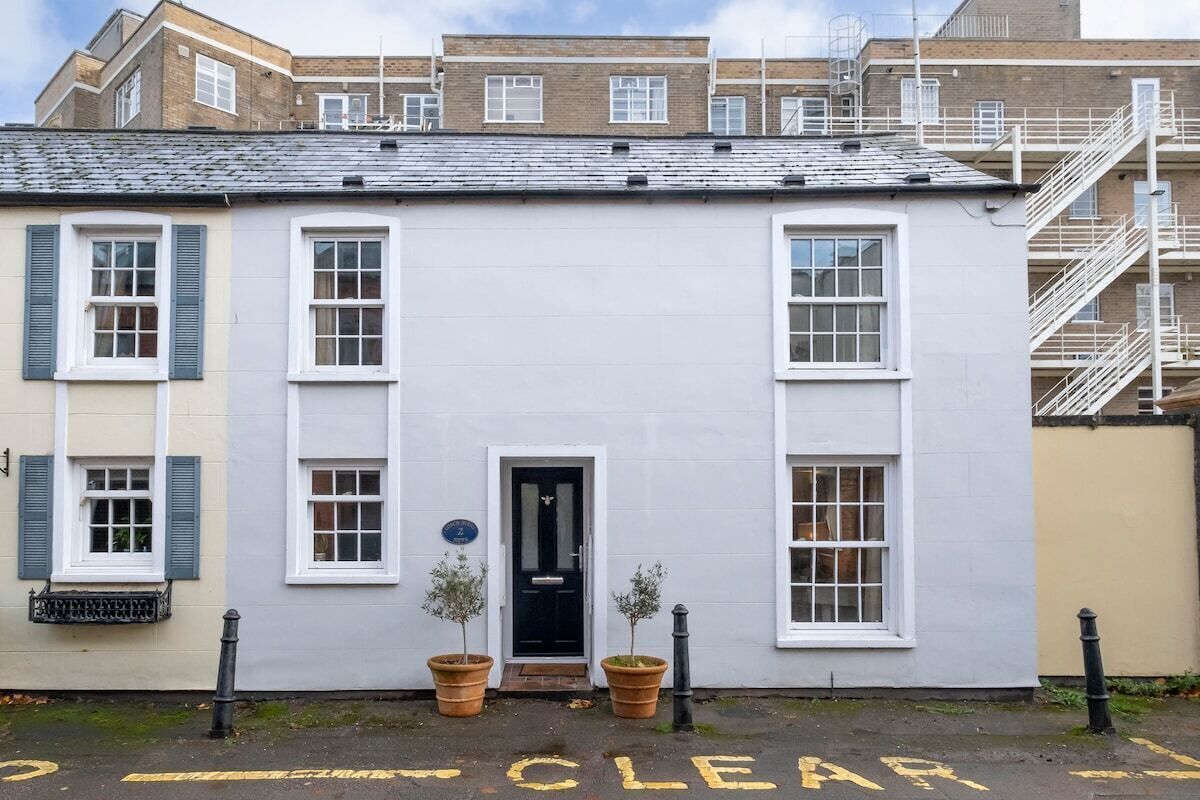A two-story building with a white facade, a black door, and two potted plants in front.