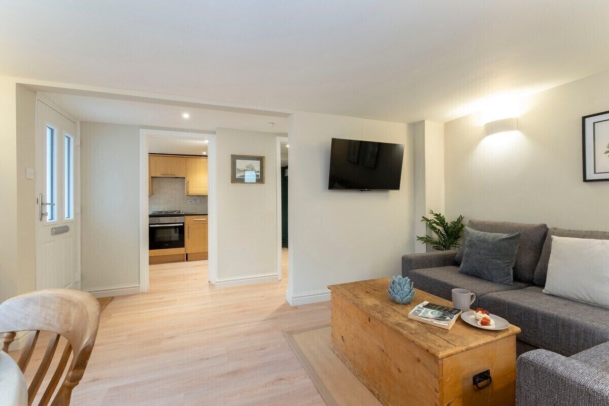 A modern living room with a grey sofa, a wooden coffee table, and a flat-screen TV mounted on the wall.