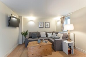 A modern living room with a grey sofa, a wooden coffee table, a mounted TV, and framed botanical prints on the wall. - Cosy Peaceful Self Contained Home in Montpellier (Cheltenham)