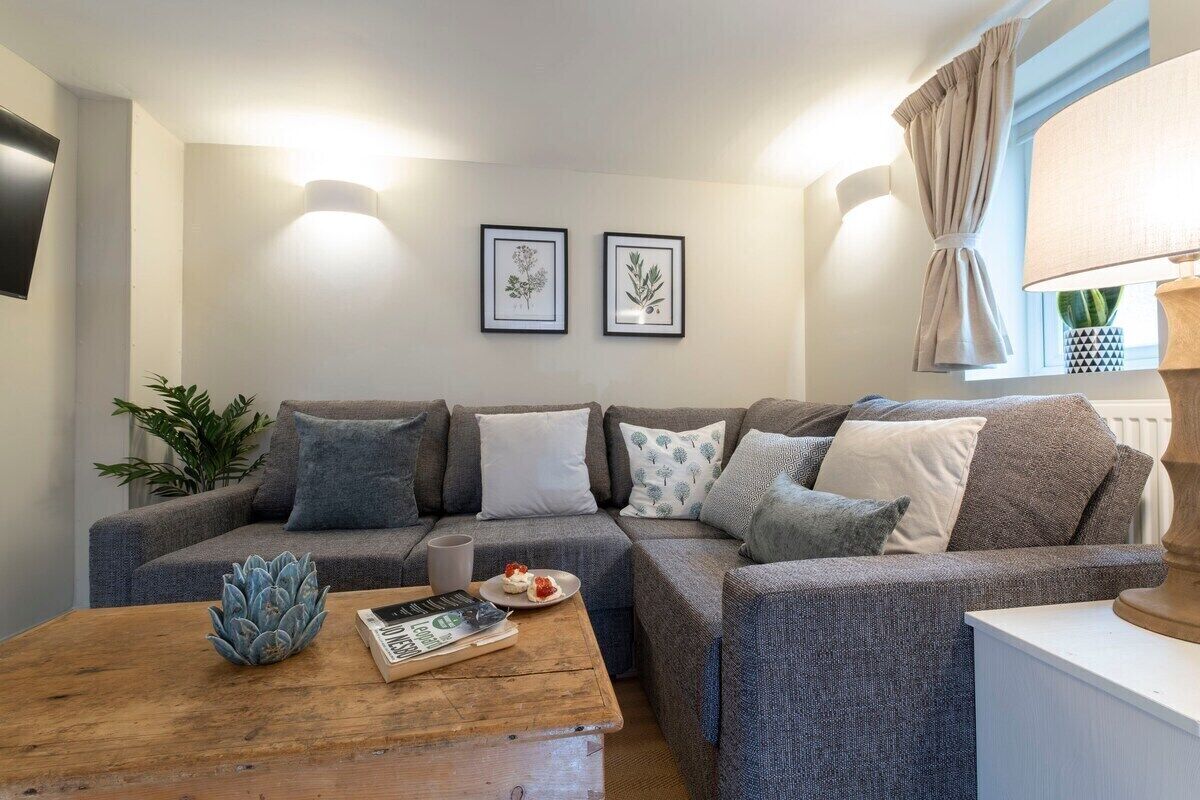 En moderne stue med en grå sofa, et træbord og indrammede botaniske tryk på væggen.