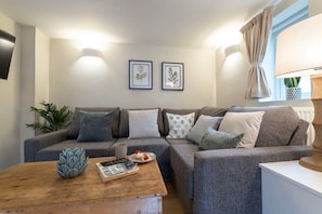 A modern living room with a grey sofa, a wooden coffee table, and framed botanical prints on the wall.