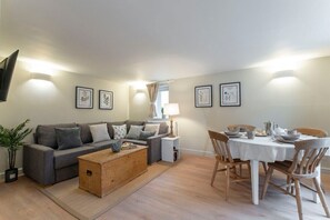 A living room with a grey sofa, wooden coffee table, dining table with chairs, and framed pictures on the wall. - Cosy Peaceful Self Contained Home in Montpellier (Cheltenham)