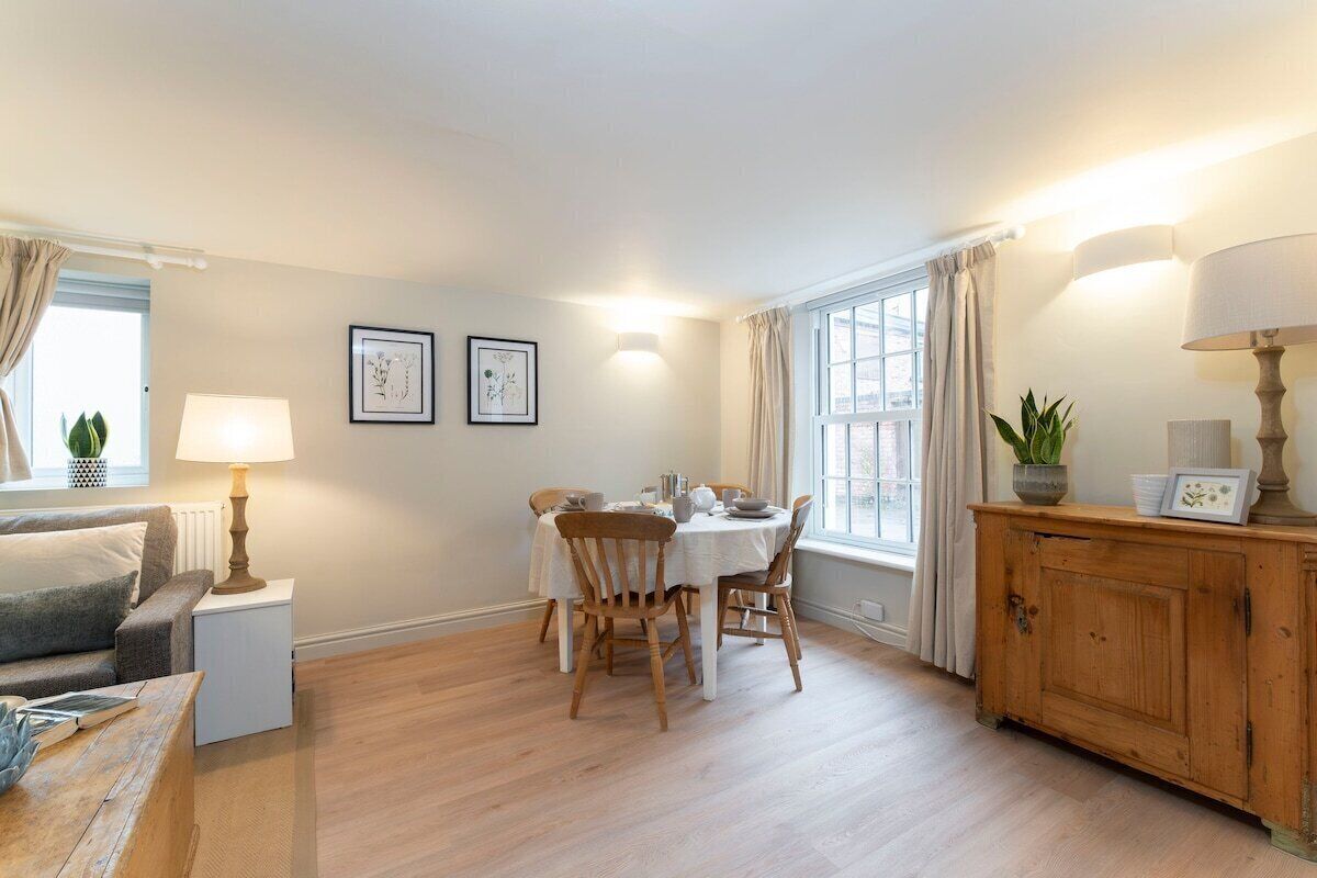 Ein gemütliches Wohnzimmer mit Esstisch, Holzstühlen, einer Couch und einem Schrank.