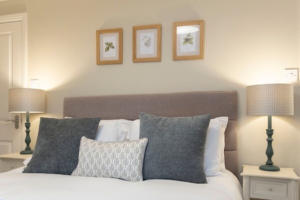 A neatly made bed with a headboard, two bedside tables with lamps, and three framed botanical prints on the wall. - Cosy Peaceful Self Contained Home in Montpellier (Cheltenham)