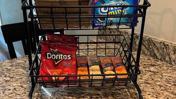 A kitchen counter with a wire rack holding various food items, including bags of chips and crackers.