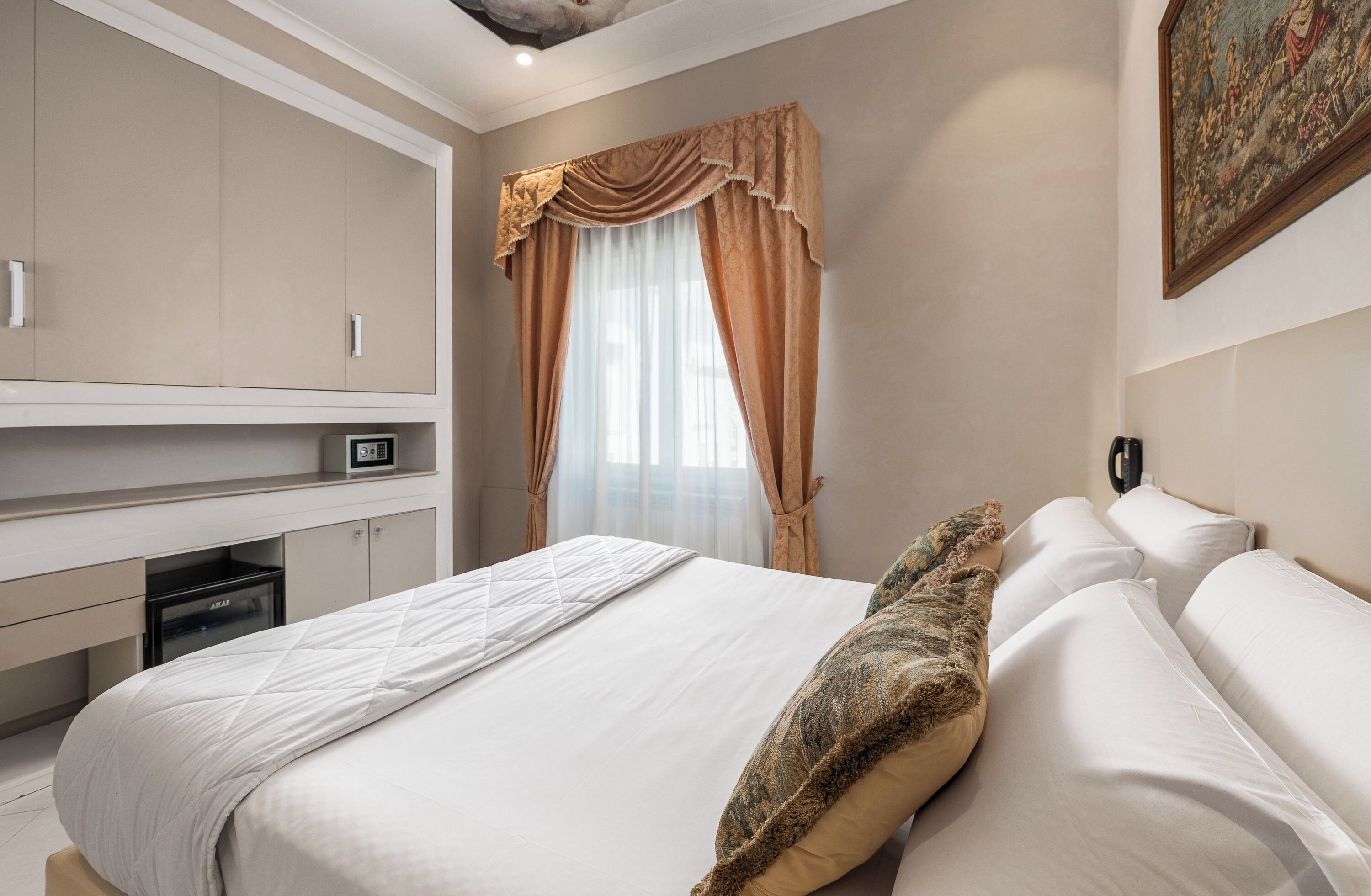 Quarto de hotel com cama, televisão, escrivaninha e janela com cortinas.