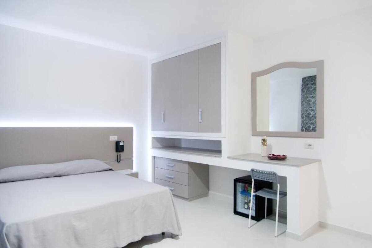 Une chambre à coucher avec un lit, un bureau avec des tiroirs, un miroir et un téléphone fixé au mur.