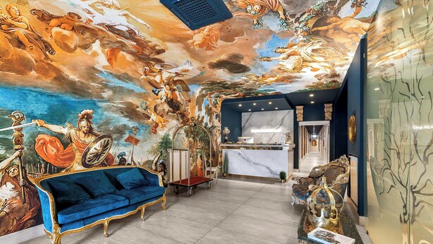 Een luxueuze lobby met een groot muurschilderij, een blauwe bank en een receptiebalie.