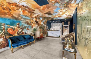 A luxurious lobby with a grand mural, a blue sofa, and a reception desk. - Hotel Regina  (Casagiove)