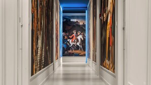 Een gang met een klassiek schilderij aan de wand, witte muren en een houten vloer.
