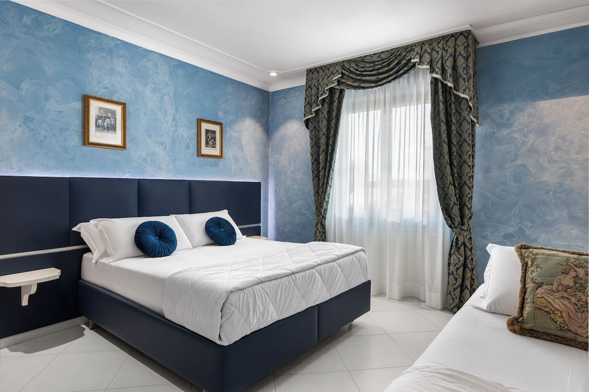 Une chambre à coucher avec un grand lit, une table de chevet et une fenêtre avec des rideaux.