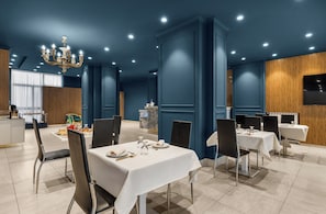 A dining area with tables set for service, a chandelier, and a television mounted on the wall. - Hotel Regina  (Casagiove)