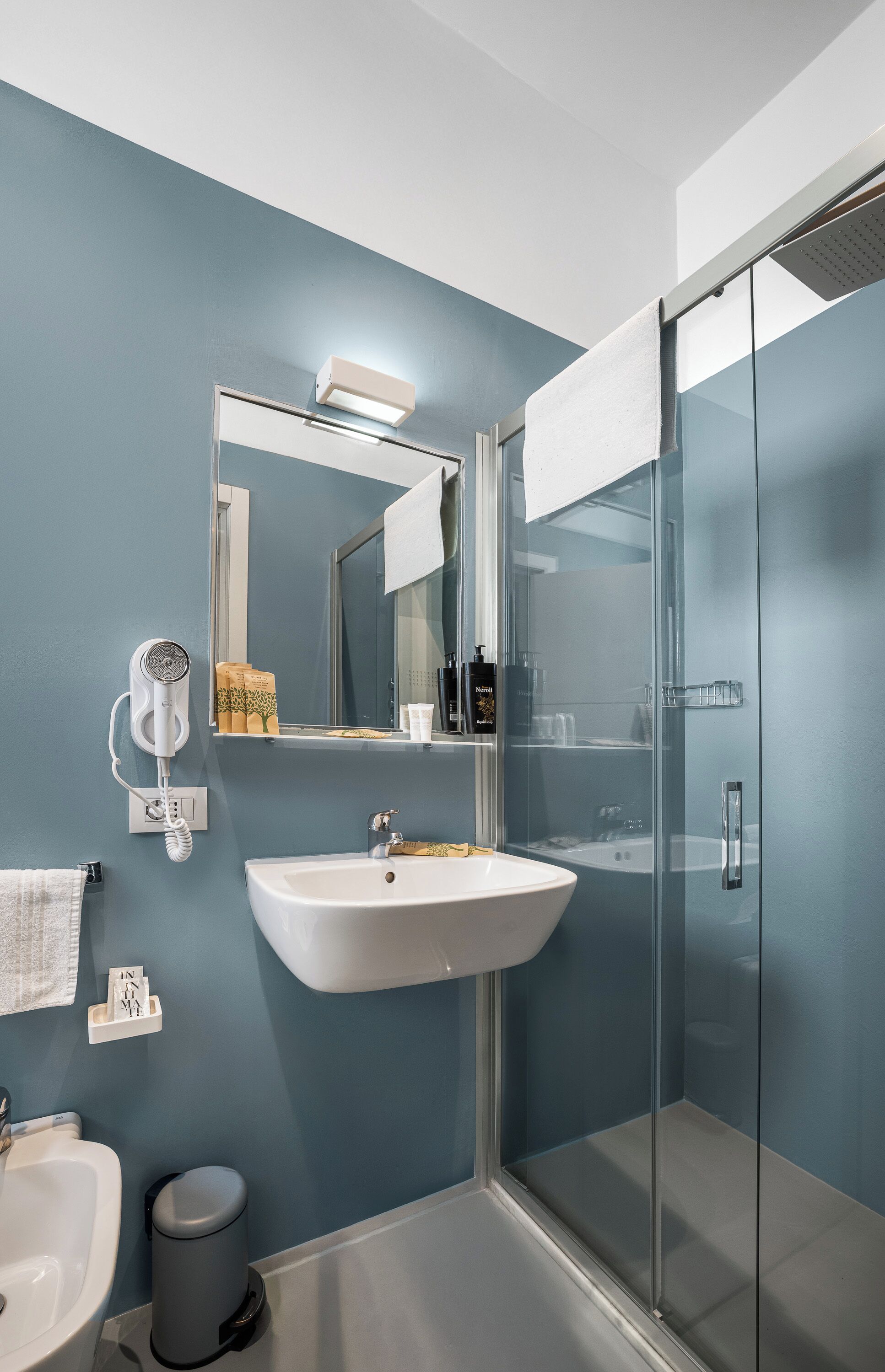 A modern bathroom with a white sink, a glass shower enclosure, and a mirror with a towel hanging on the wall.