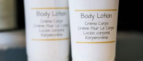 Two white tubes of body lotion with gold decorative patterns and text in multiple languages.