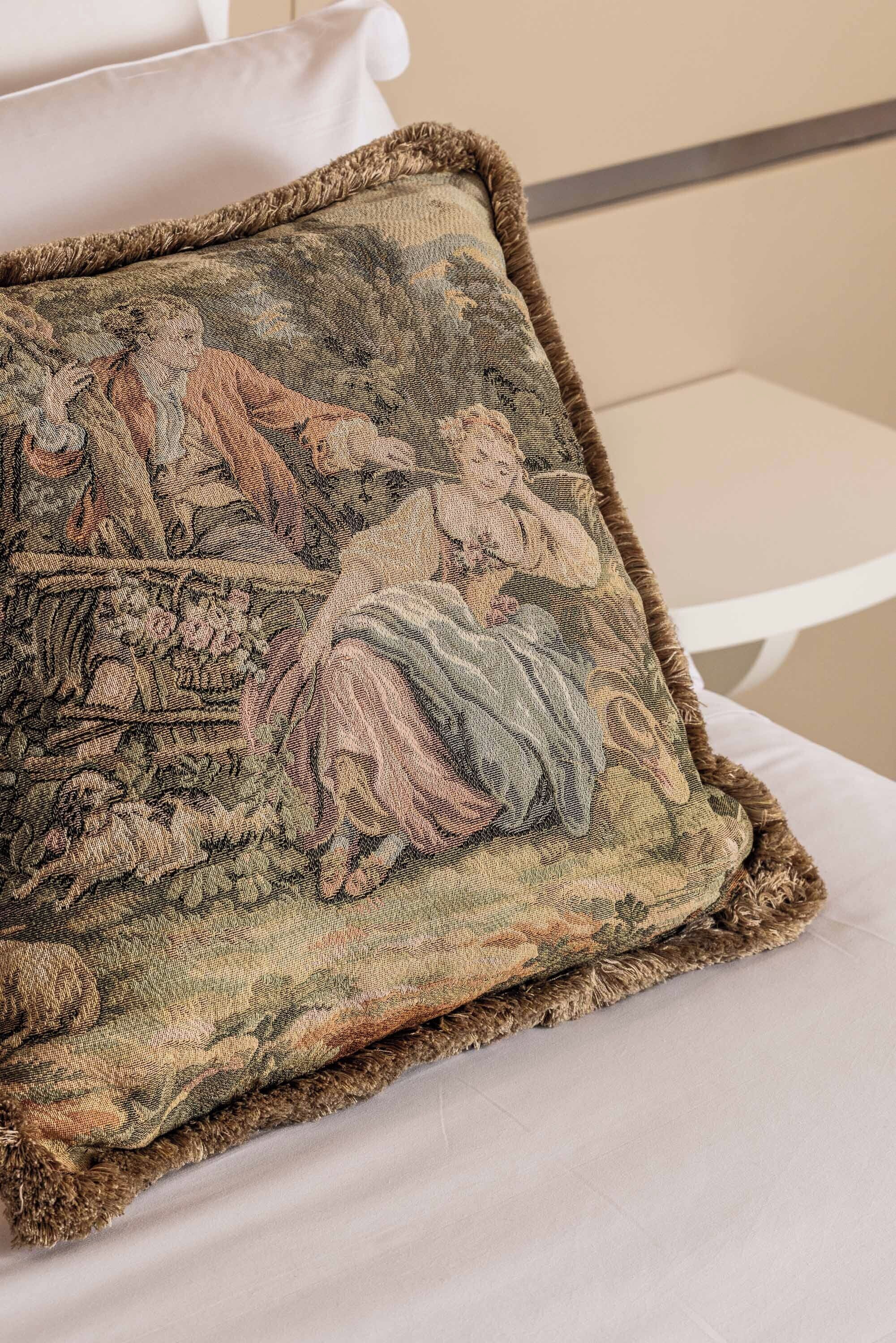 A bed with a decorative pillow featuring a detailed tapestry design.