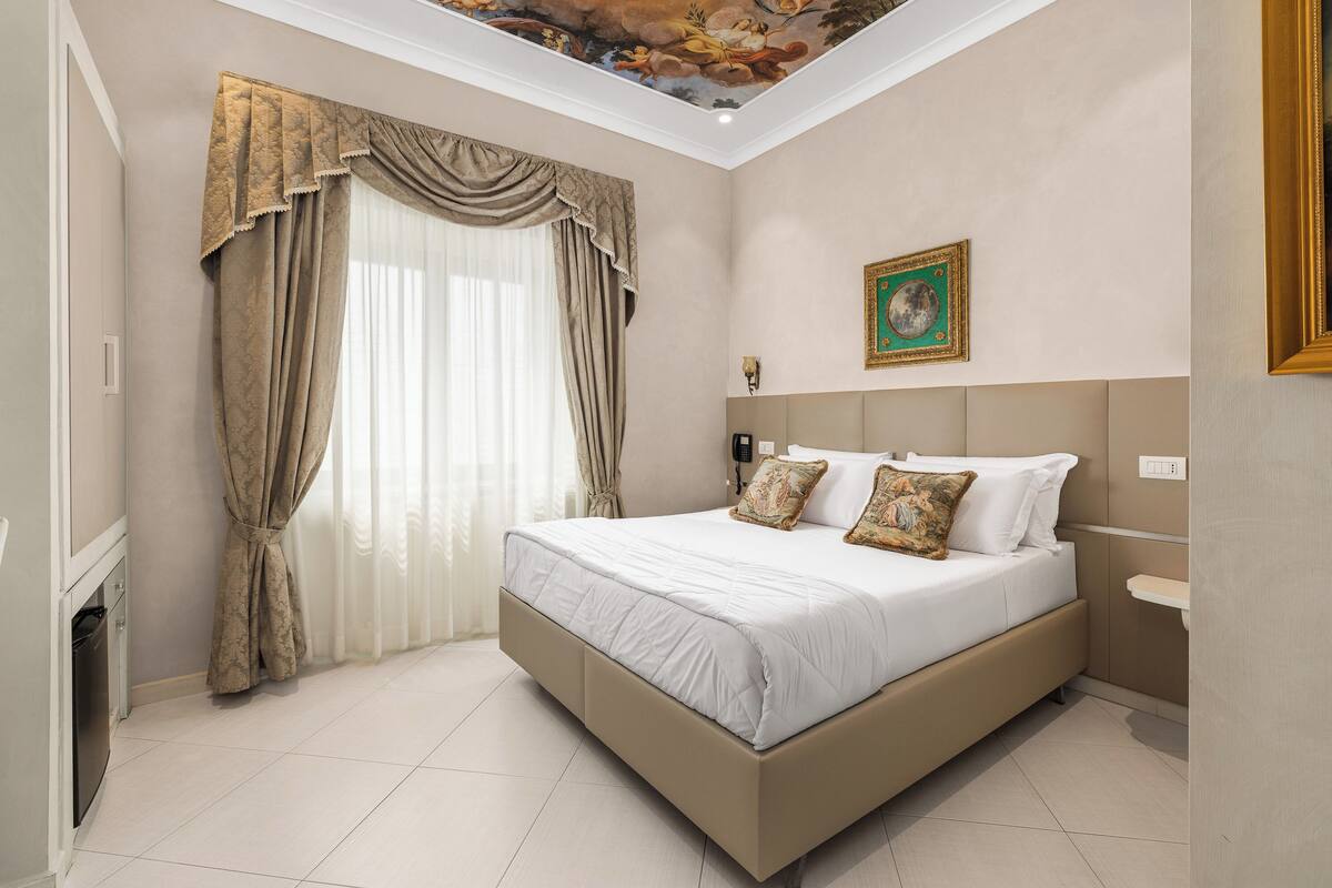 Une chambre à coucher avec un lit, des rideaux, un tableau, une table de chevet et une commode.