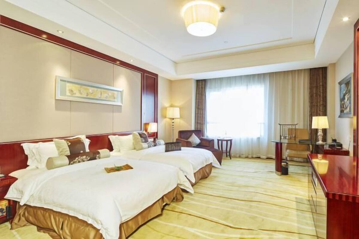 Ein Hotelzimmer mit zwei Betten, einem Schreibtisch, einem Stuhl, einer Lampe und einem Bild an der Wand.