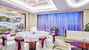 A banquet hall with a round table set for a formal event, surrounded by chairs with white covers and purple sashes.