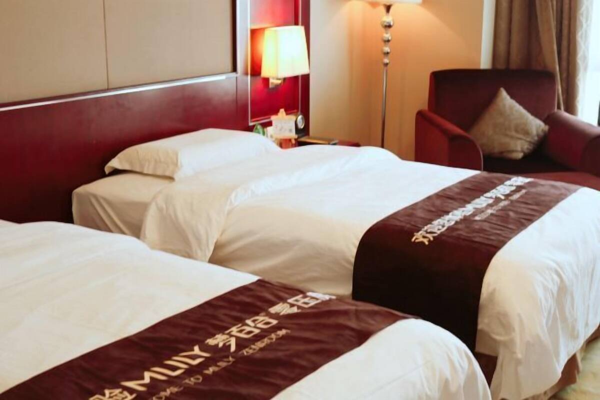 Ein Hotelzimmer mit zwei Betten, einer roten Wand, einer Lampe und einem Sessel.