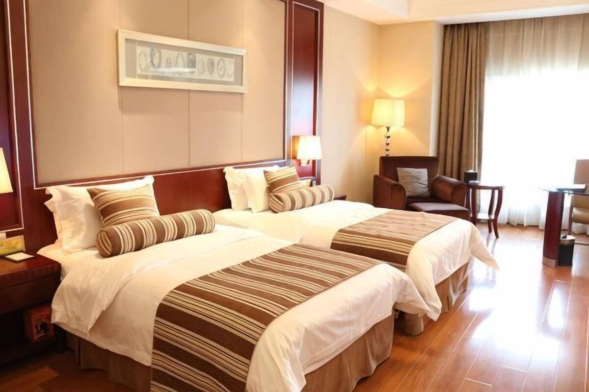 Ein Hotelzimmer mit zwei Betten, einem Schreibtisch, einem Sessel, einer Lampe und einem Bild an der Wand.