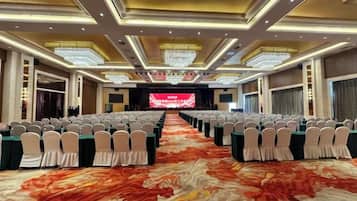 A banquet hall with rows of tables and chairs, a stage with a large screen, and a patterned carpet.