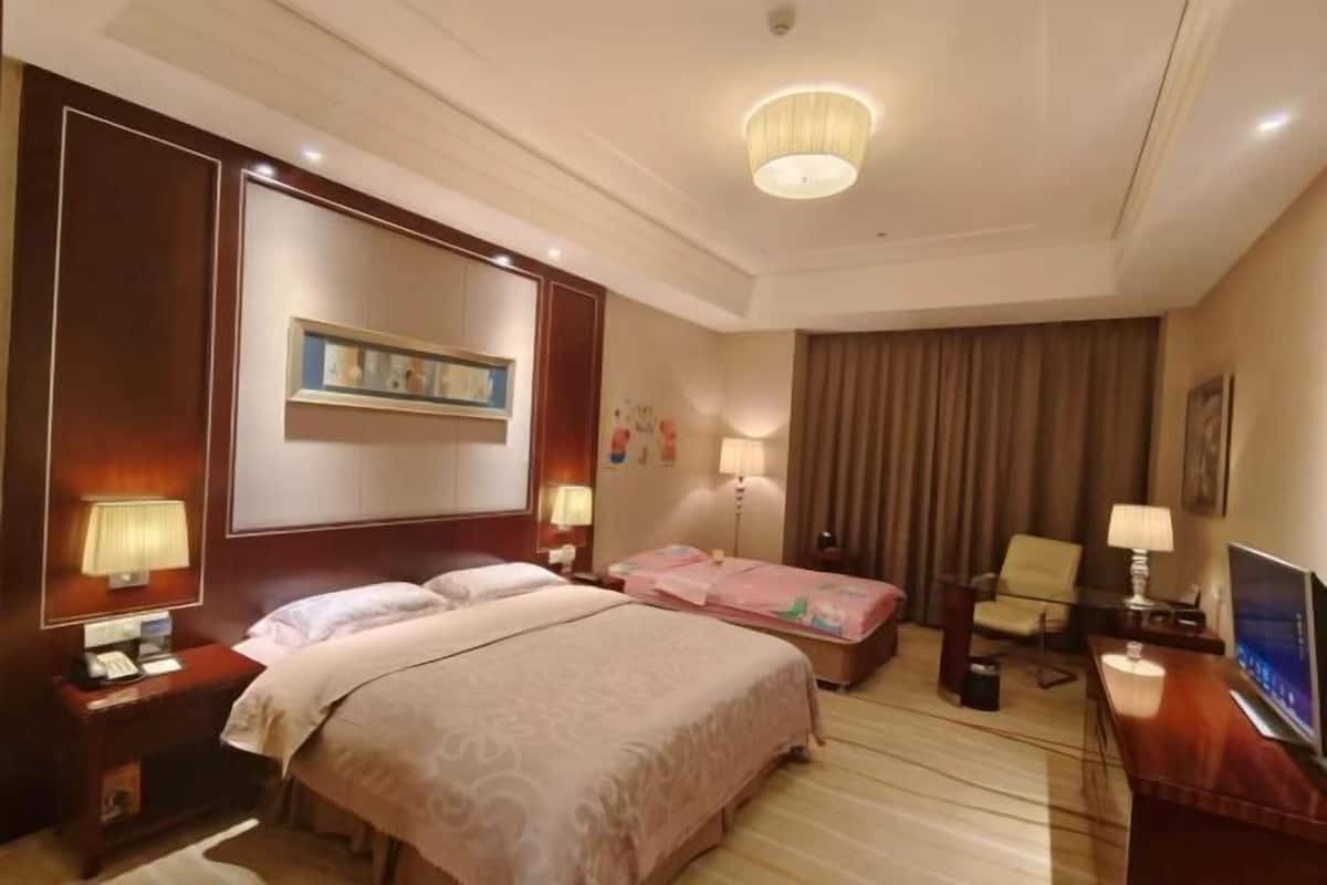 Ein Hotelzimmer mit einem großen Bett, Nachttischen mit Lampen, einem Schreibtisch mit Fernseher und einem großen Fenster mit Vorhängen.
