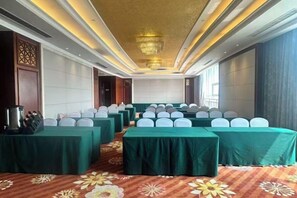 Une salle de conférence avec des rangées de tables, de chaises et un lustre.