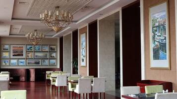 A hotel lobby with a long reception desk, multiple dining tables, and chairs.
