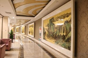 Een hotelgang met een lange hal, kunstwerken aan de muur en een zithoek met een stoel.