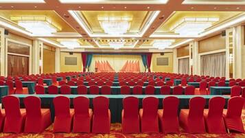 A conference room with rows of tables and chairs, a stage with curtains, and a chandelier.
