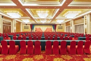 Een congreszaal met rijen tafels en stoelen, een podium met gordijnen en een kroonluchter.