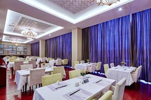A banquet hall with multiple tables, chairs, and a chandelier.