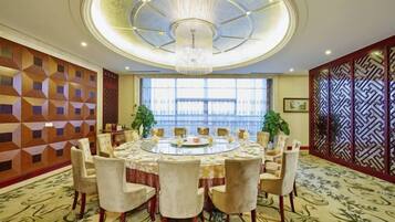 Un salón de conferencias con una mesa redonda, sillas, un candelabro, paredes con diseño y ventanas amplias.