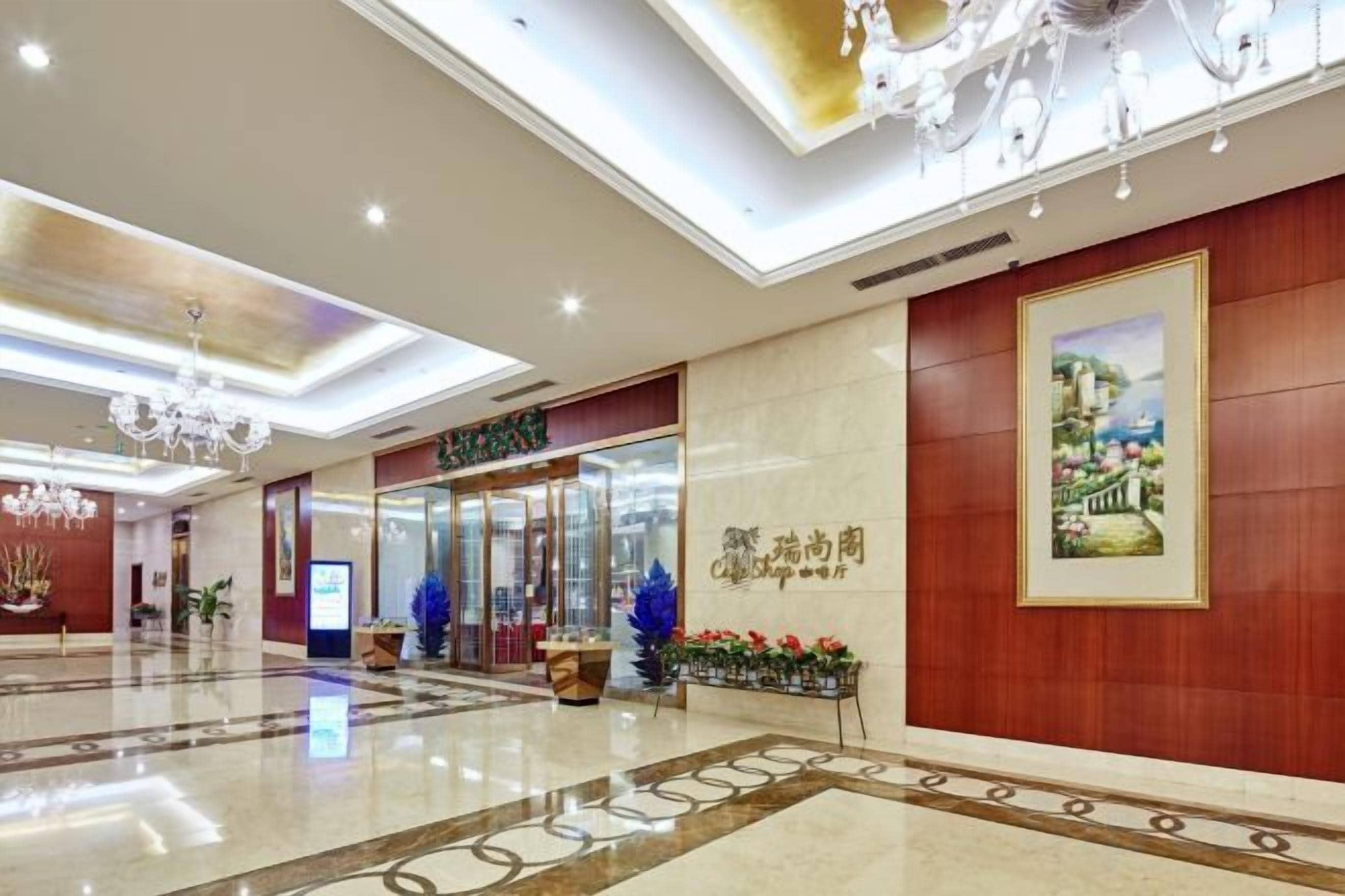 A hotel lobby with a reception desk, a framed artwork, and a chandelier.
