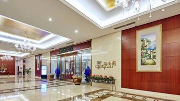 A hotel lobby with a reception desk, a framed artwork, and a chandelier.