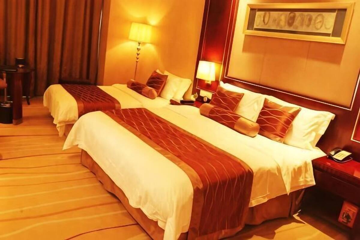 Ein Hotelzimmer mit zwei Betten, einem Schreibtisch, einer Lampe und einem gerahmten Bild an der Wand.