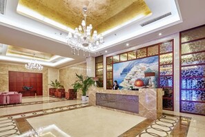 A hotel lobby with a marble reception desk, a chandelier, and a large painting of a coastal scene.