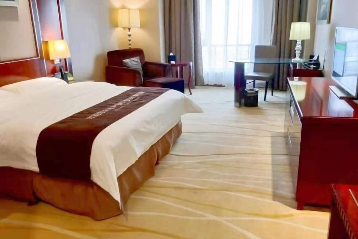 Ein Hotelzimmer mit einem großen Bett, einem Schreibtisch, einem Sessel und einem Fernseher.