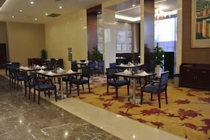 A hotel lobby with multiple dining tables and chairs, a carpeted floor, and a reception desk. - Jimo Huaxi Hotel (Qingdao)