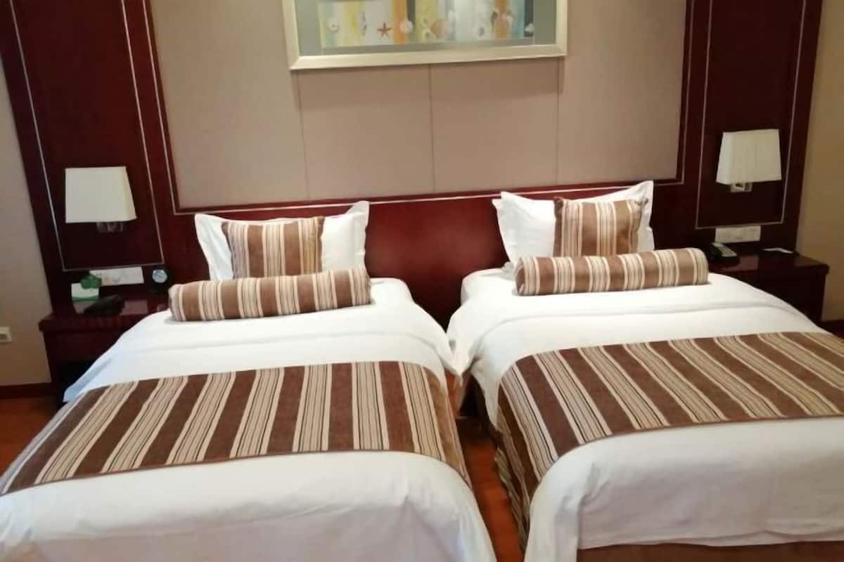 Ein Hotelzimmer mit zwei Betten, jeweils mit gestreifter Bettwäsche und Kissen, einem hölzernen Kopfteil, Nachttischlampen und einem Bild an der Wand.