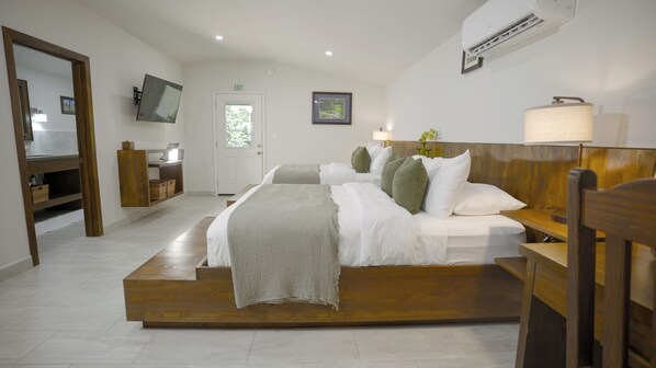 A bedroom with a large bed, bedside tables, a TV, and an air conditioning unit. - Roaring River Resort (Belmopan)