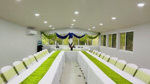 A conference room with long tables, white chairs, and green sashes. - Roaring River Resort (Belmopan)