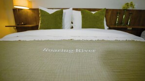 A neatly made bed with a green and white bedspread and pillows, a wooden headboard, and a bedside table with a lamp. - Roaring River Resort (Belmopan)
