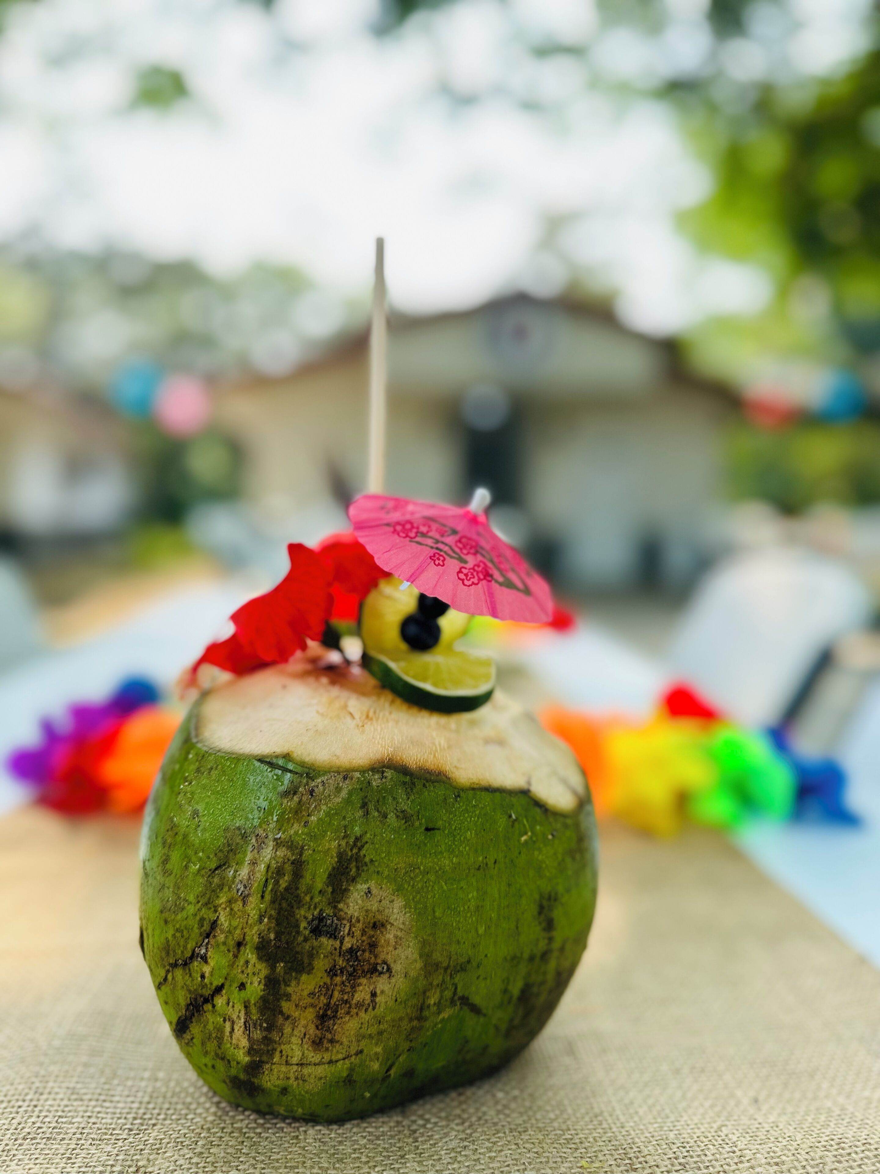 A coconut with a lime slice and a pink umbrella on top, placed on a textured surface.