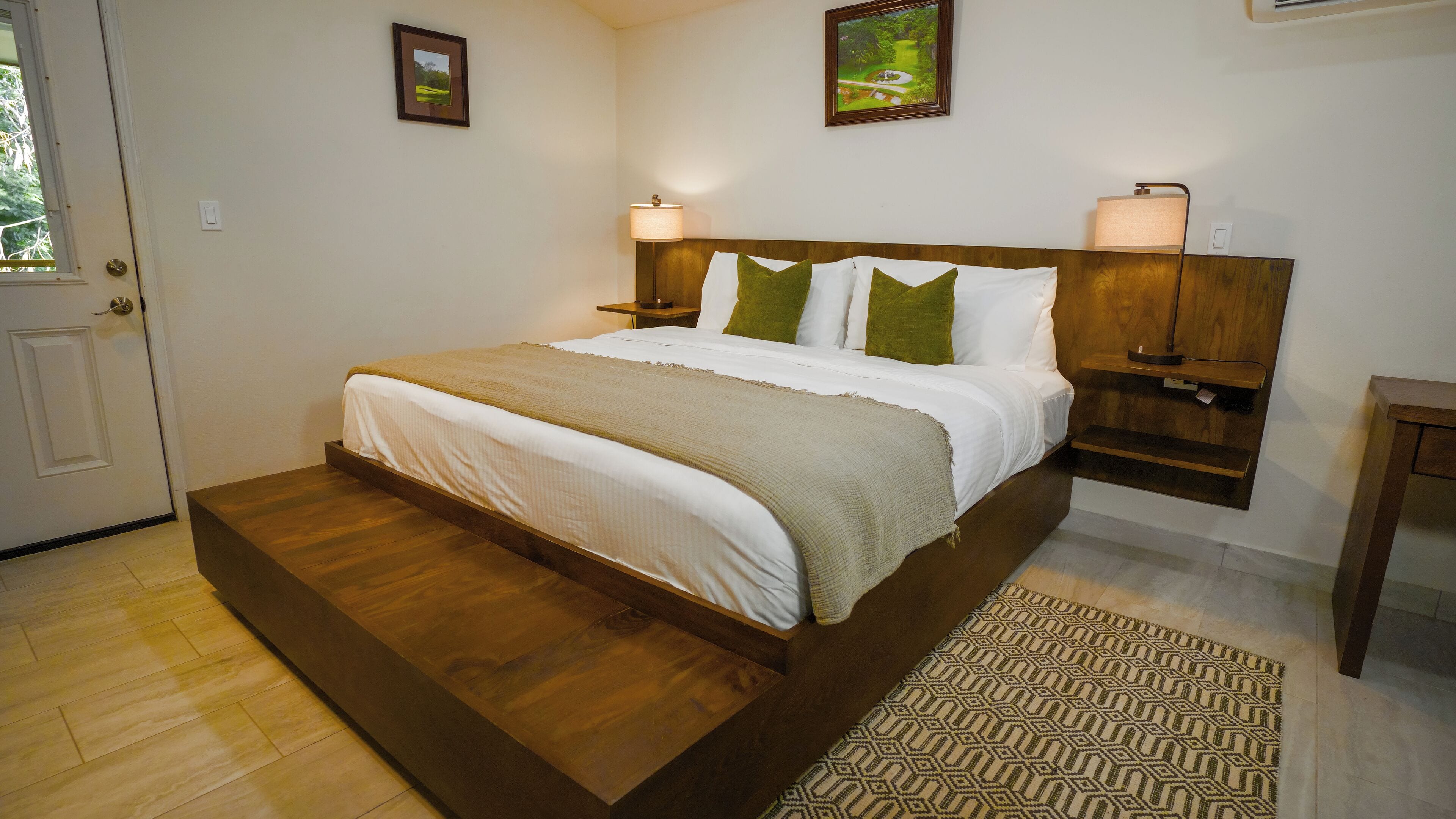 Un dormitorio con una cama de madera, dos lámparas de noche, una puerta y un cuadro en la pared.