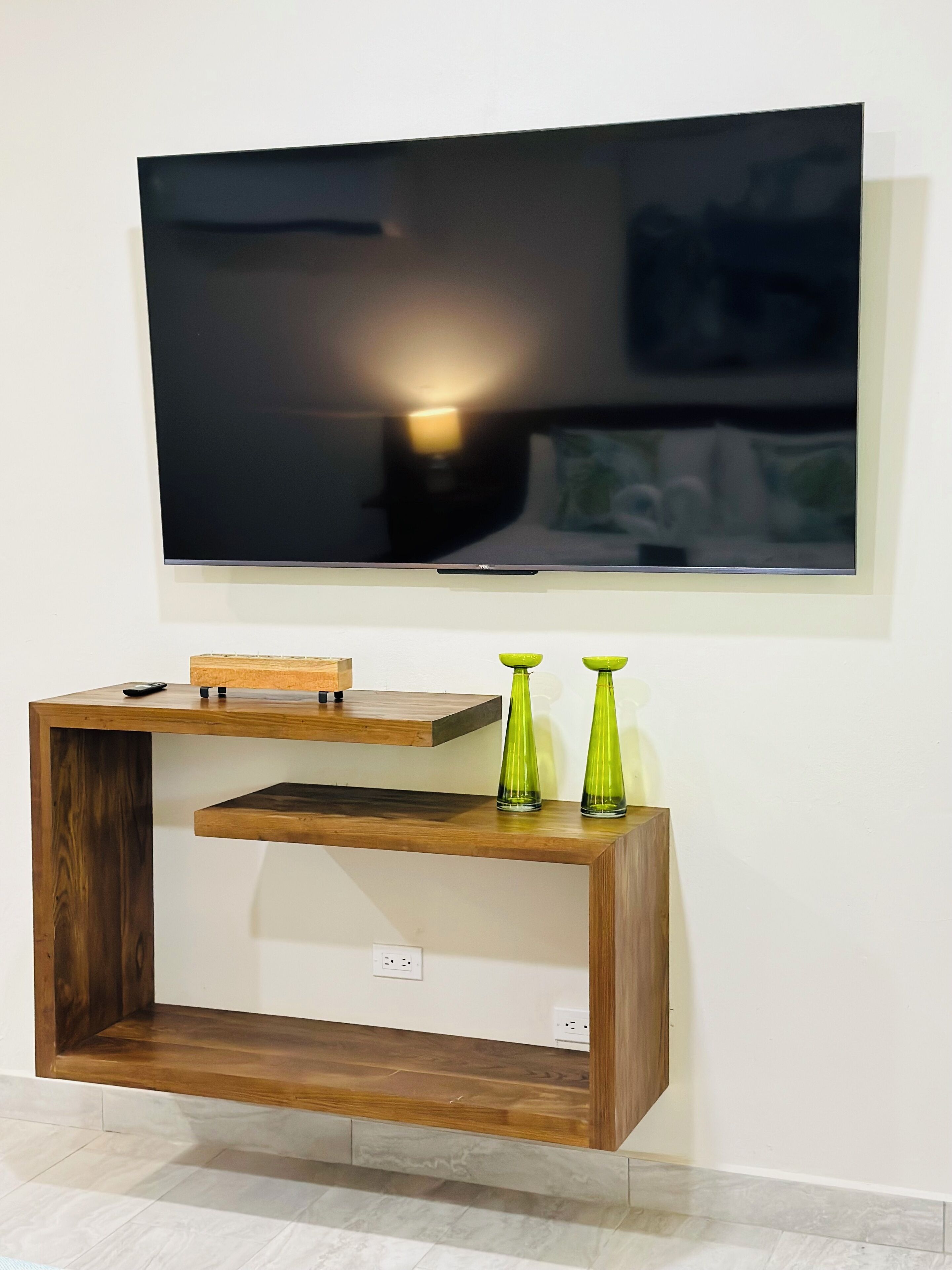 Een flatscreen televisie hangt aan de muur boven een houten dressoir met twee groene vazen.
