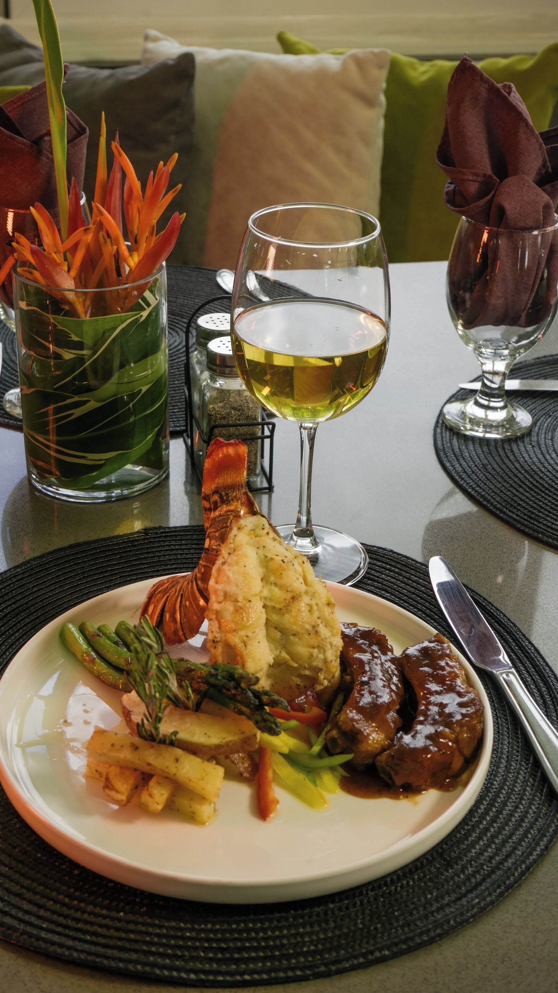 A dining table with a lobster dish, asparagus, and a glass of white wine.