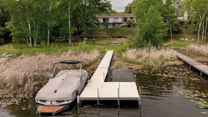 Un bateau était amarré à une jetée en bois qui s’étendait sur une étendue d’eau, entourée d’une végétation luxuriante et avec un bâtiment visible au loin.